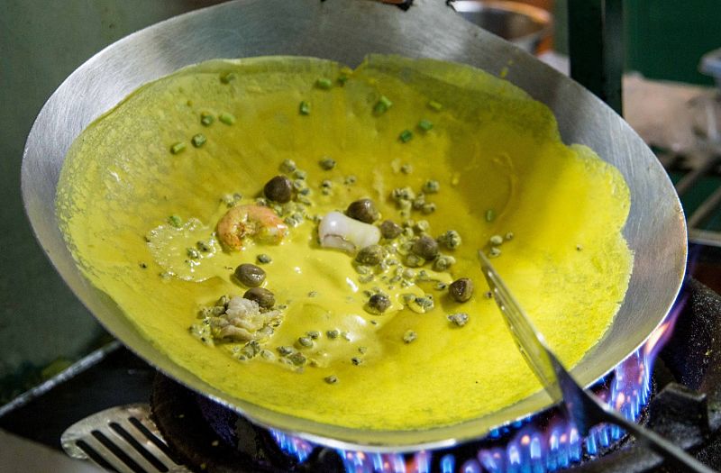 bahn xeo pancake being cooked in a wok over a gas burner set to a high heat